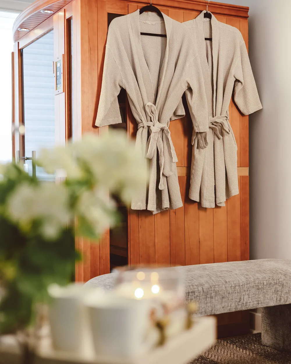 Two robes hanging on a wooden cabinet in the Revive clinic, with a cup and greenery in the foreground.