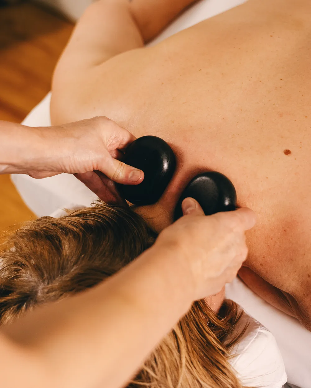 A therapist using two smooth black stones on a client’s upper back at Revive.