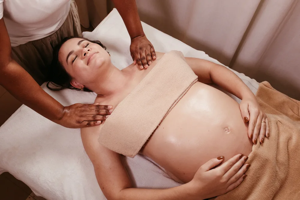 A pregnant client receiving a shoulder massage while resting on a treatment table.