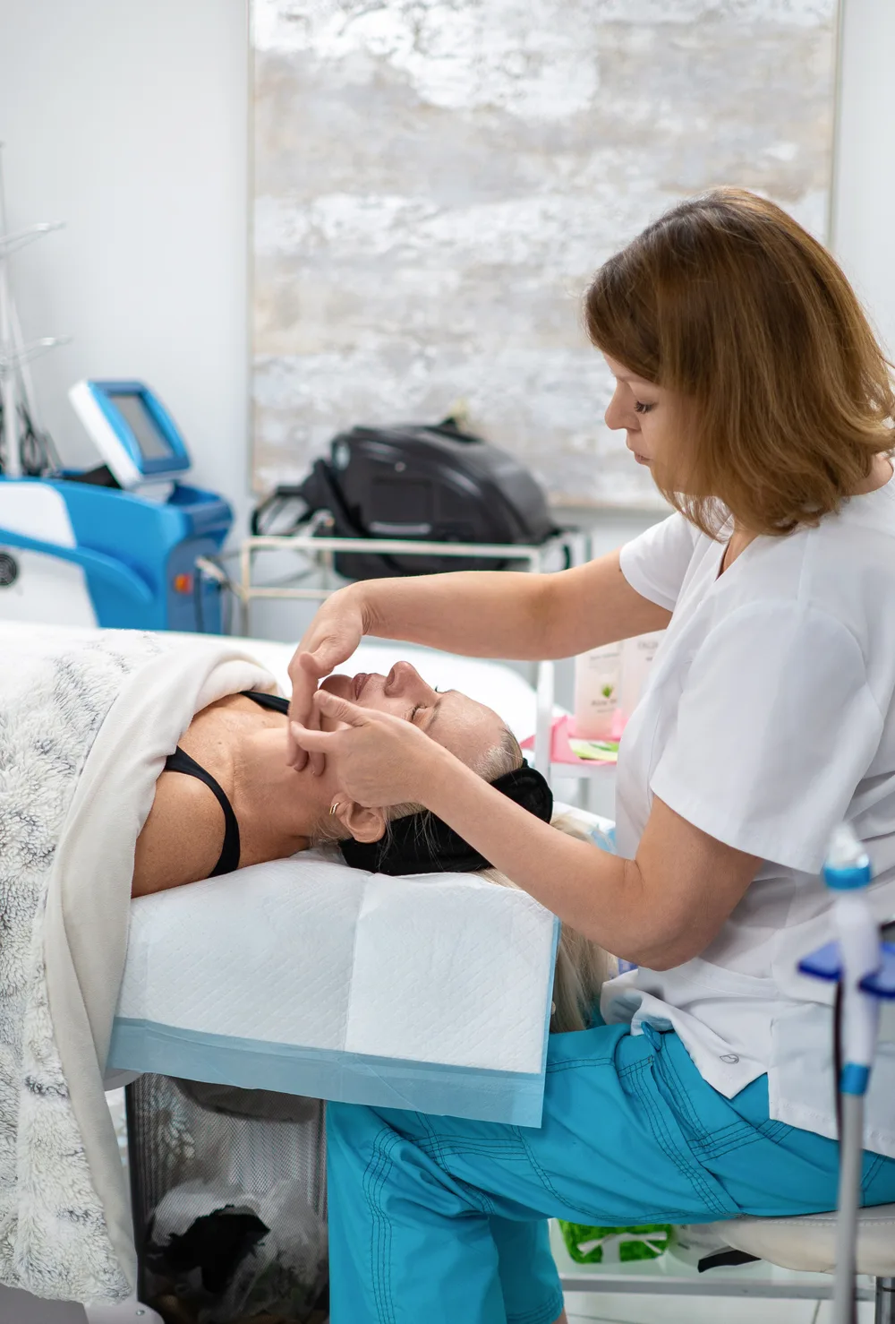 A therapist working with her hands along a reclining client’s jaw and face.